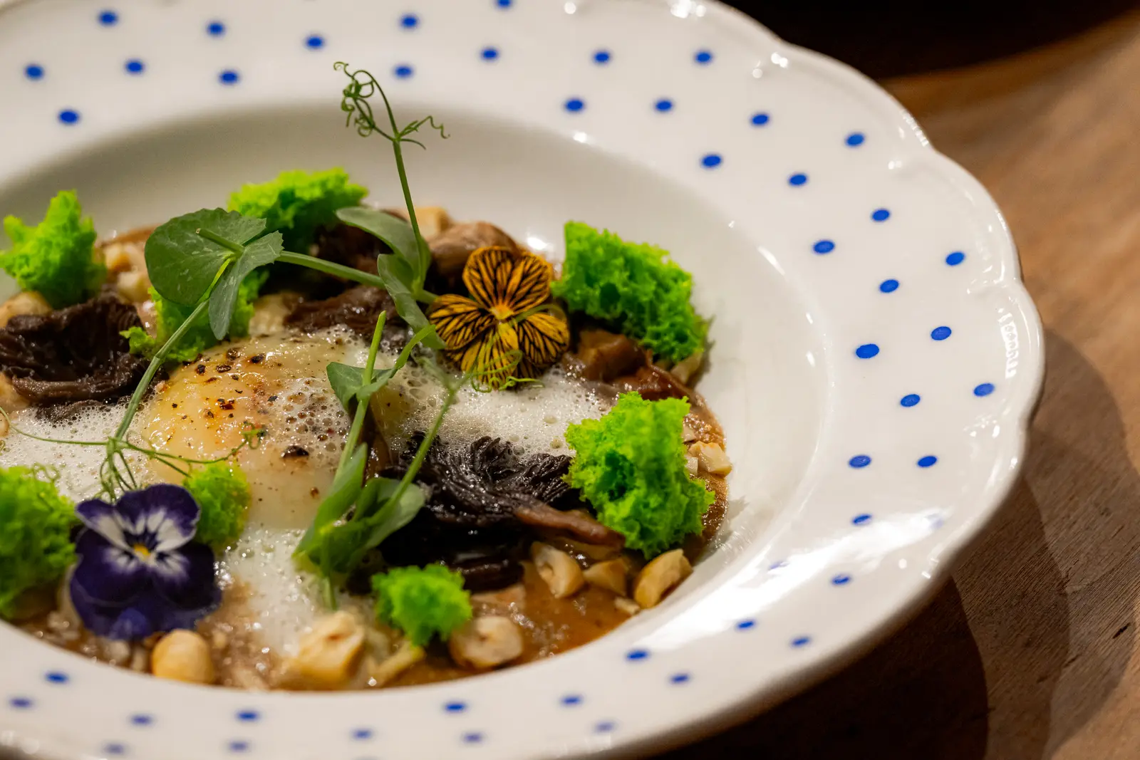 Une assiette creuse à pois bleus : œuf, champignons, mousse, éclats de noisette, pousses et pensées comestibles.