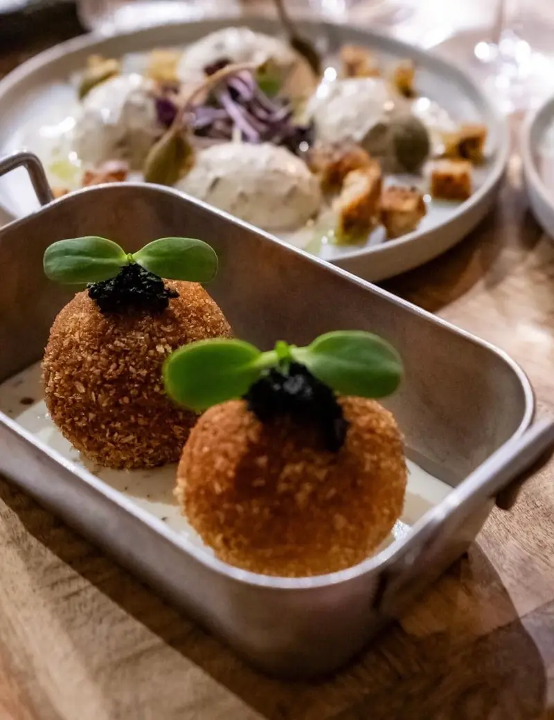 Deux croquettes dorées garnies de pousses vertes, dans un plat en métal.