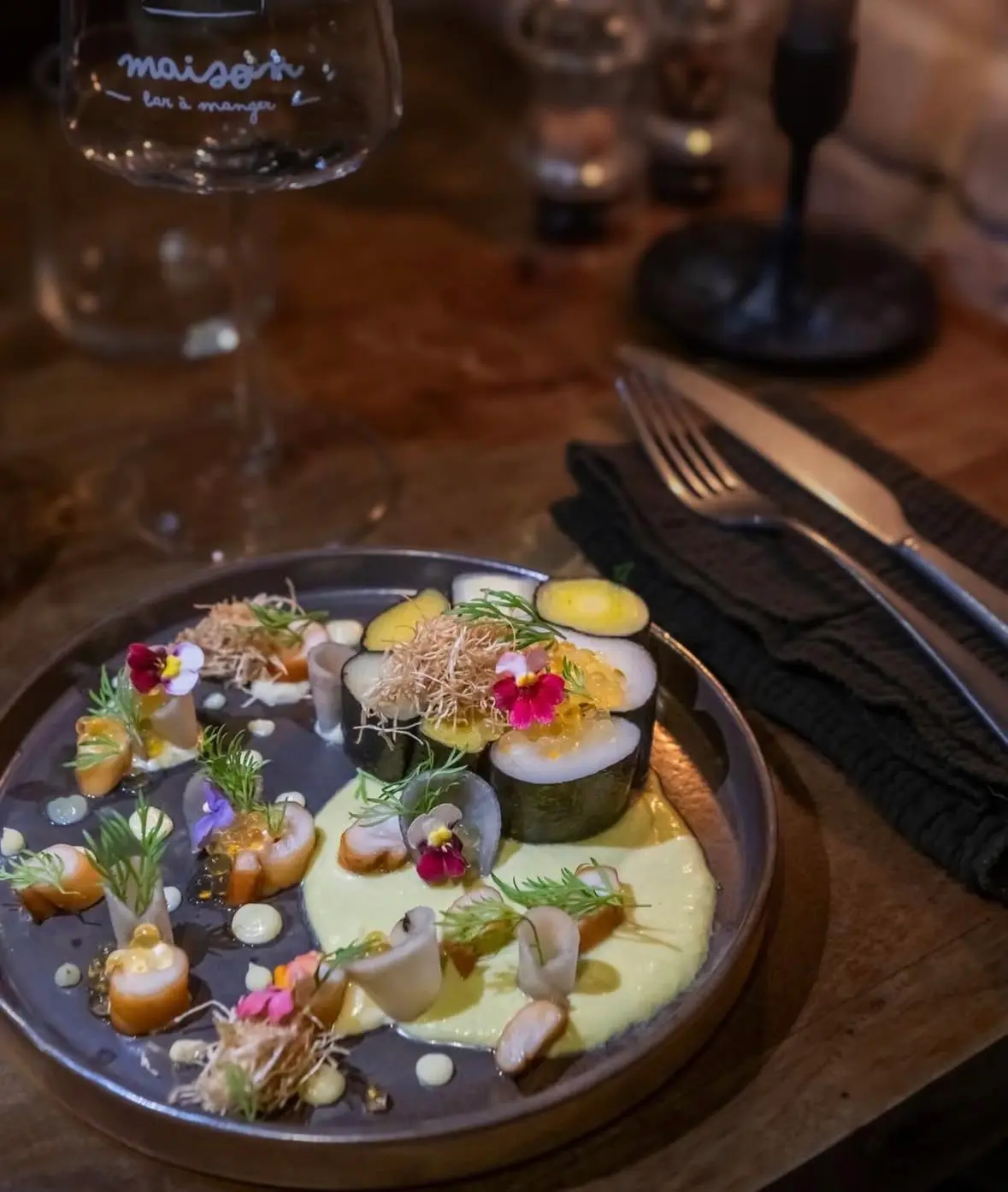Une assiette de petites bouchées colorées et de fleurs comestibles, posée sur une table en bois.