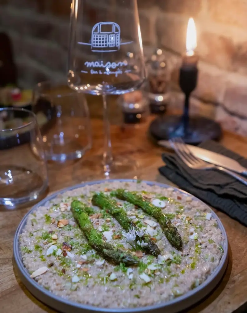 Un risotto crémeux surmonté d'asperges vertes, à côté d'un verre gravé du logo maison.