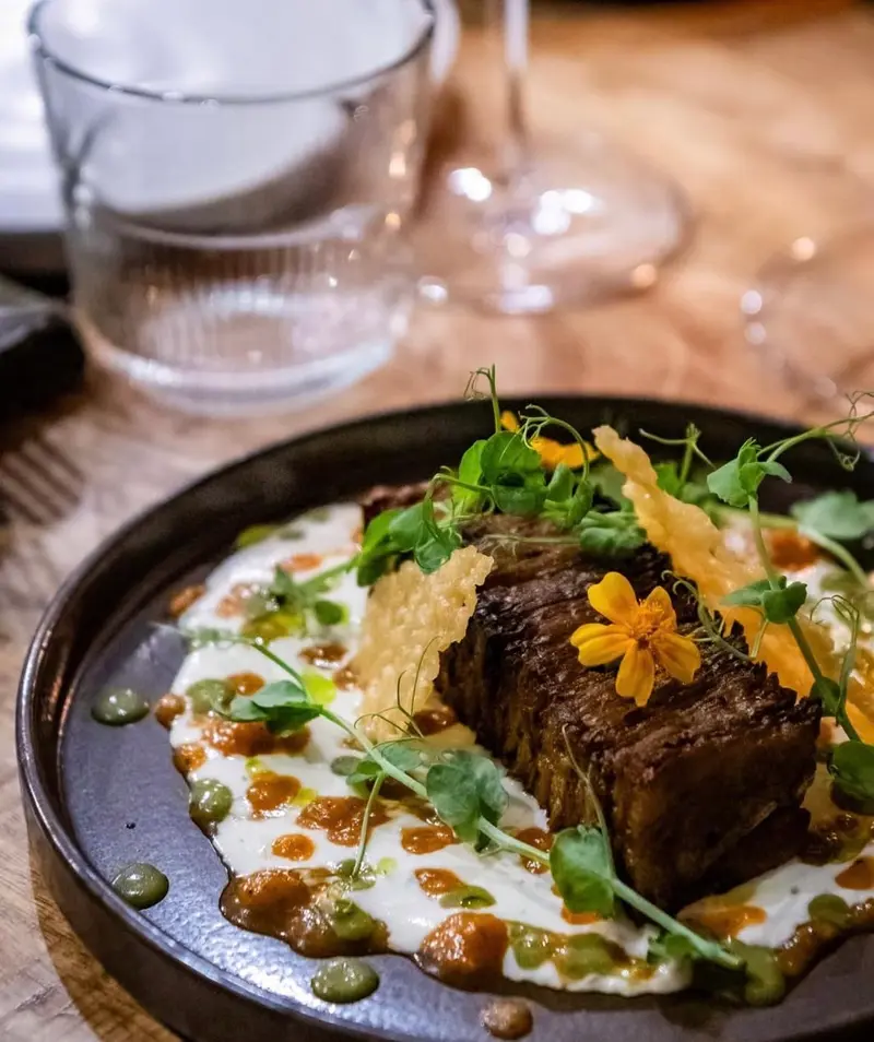 Une pièce de viande fondante sur une crème, parsemée de fleurs jaunes et d'herbes.